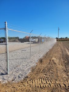 A chain link fence stands in the center of a dirt field, representing commercial fencing in an open area.
